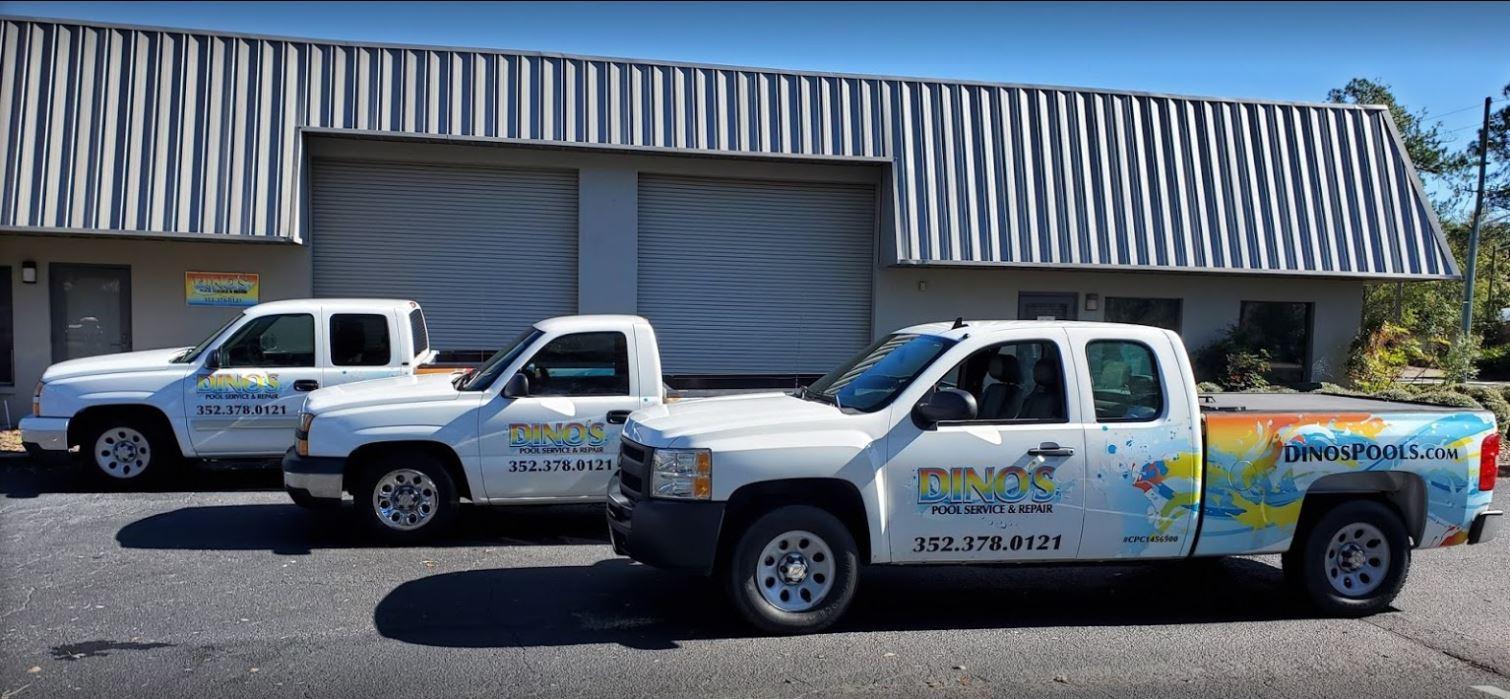 Two white Dinos trucks sitting in front of a garrage